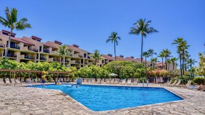 A swimming pool with lounge chairs and palm trees, surrounded by a building with balconies. - KAMAOLE SANDS 7402, REMODELED, AC, PARTIAL OCEAN, KAMAOLE BEACH PARK! (Kihei)