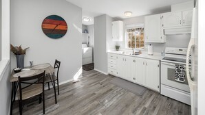 Uma cozinha moderna com armários brancos, uma mesa de jantar de madeira e um relógio colorido na parede.