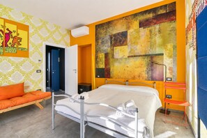 Quarto de hotel moderno com cama, sofá, banheiro e uma grande pintura abstrata na parede.