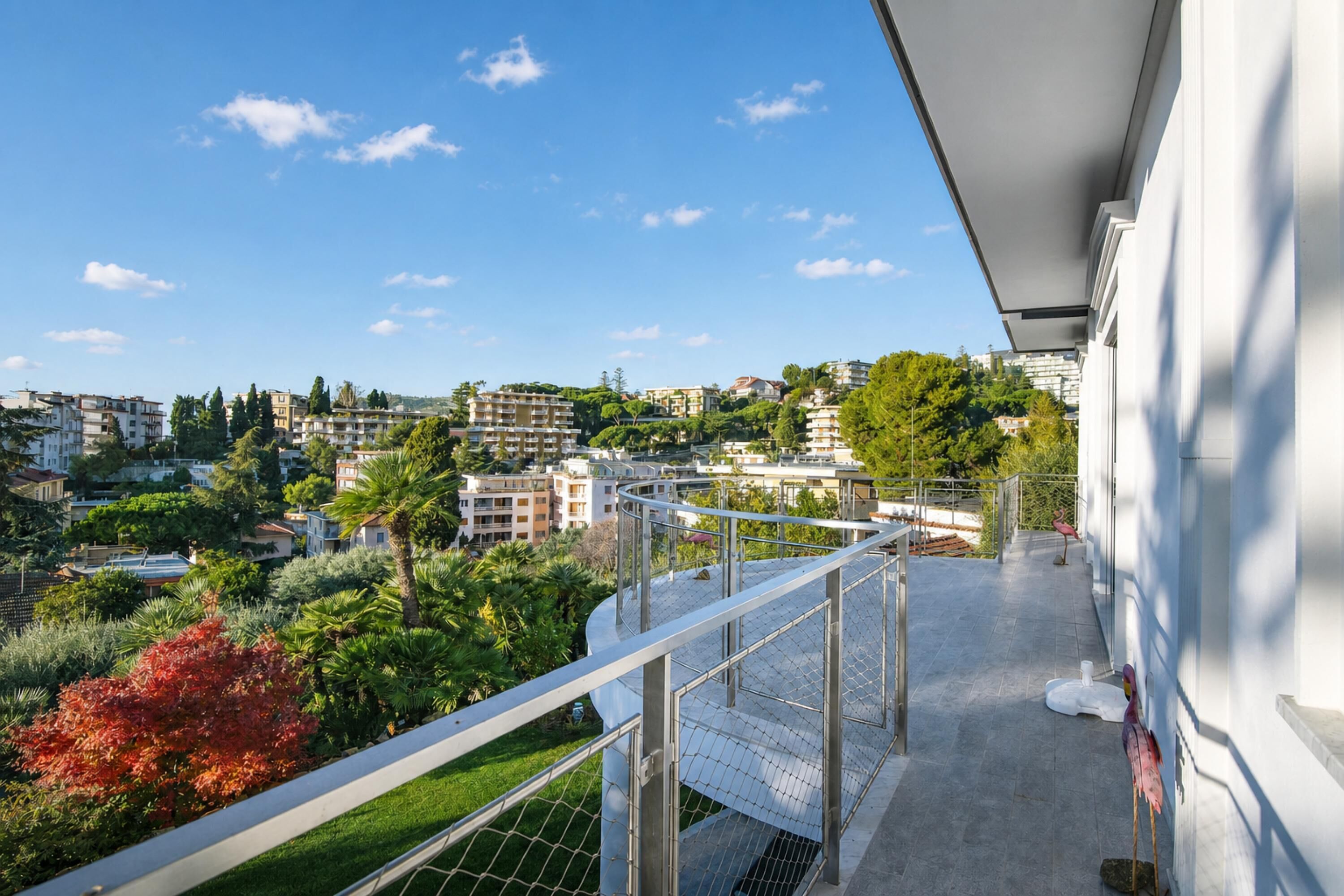 Un balcone con ringhiera in metallo che si affaccia su una zona residenziale con edifici e alberi.