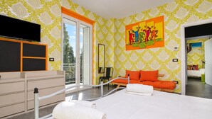 Ett modernt hotellrum med en stor säng, en sittgrupp med orange kuddar, en tavla på väggen och utsikt över omgivningarna.