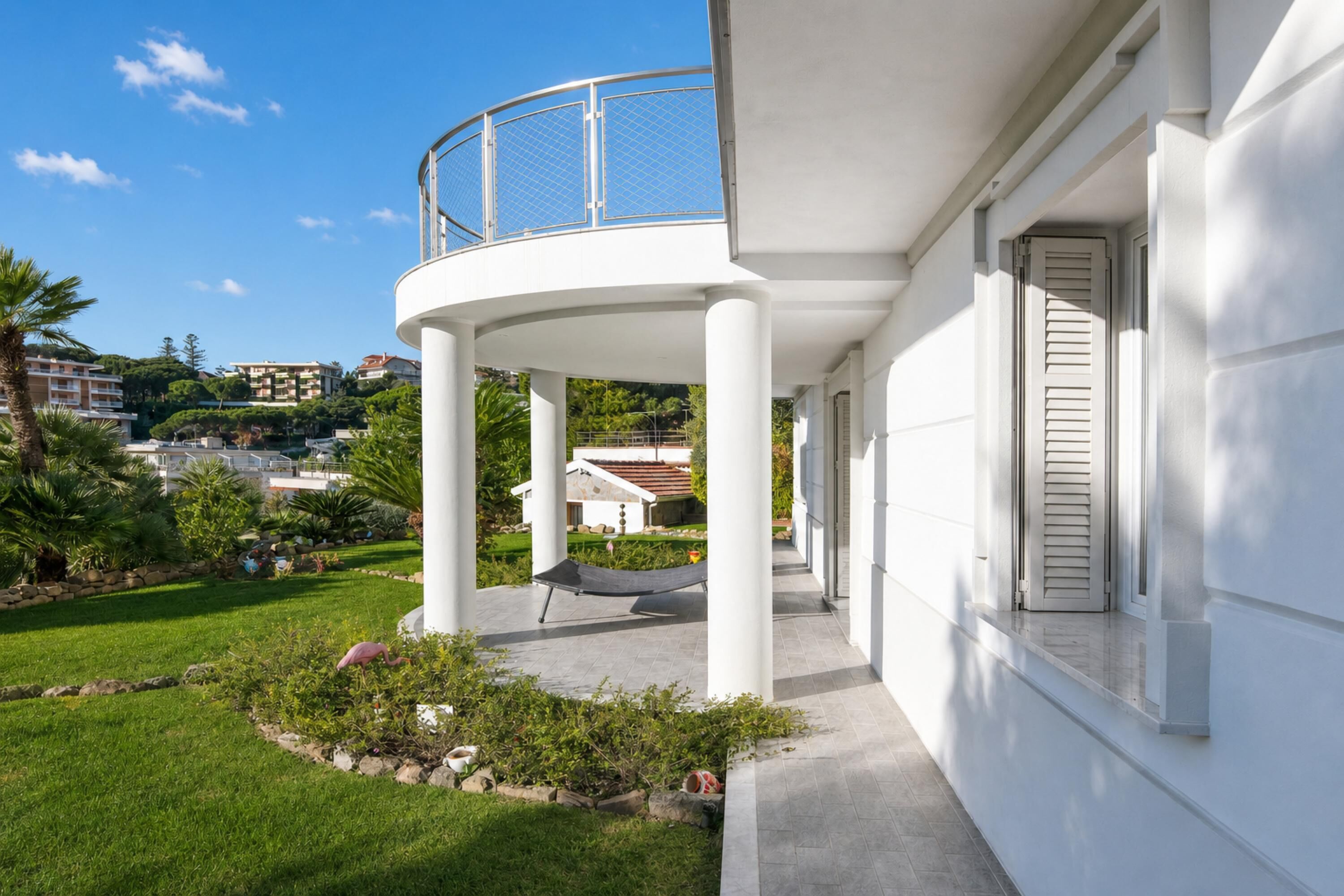 A modern building with a covered outdoor area, a curved balcony, and a garden with a hammock.