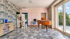 Ett rum med ett mönstrat golv, ett piano, ett stort fönster och en vägg med en tapet som föreställer en stadsbild.
