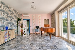 Une pièce avec un sol à motifs, un piano, une grande fenêtre et un mur recouvert d’un papier peint représentant un paysage urbain.