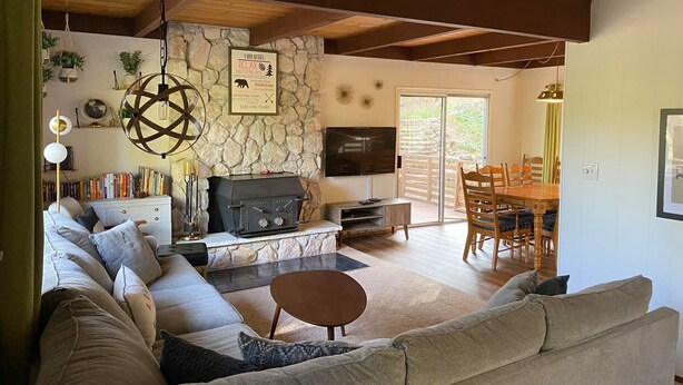 Un salon chaleureux avec un mur en pierre, une cheminée, un téléviseur et un coin repas doté de meubles en bois.