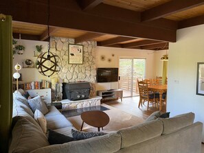 A cozy living room with a stone wall, a fireplace, a TV, and a dining area with wooden furniture.