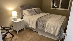 Un dormitorio con cama, mesita de noche con lámpara, ventana y puerta.