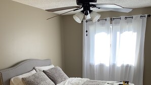 Un dormitorio con cama, mesita de noche y ventilador de techo.