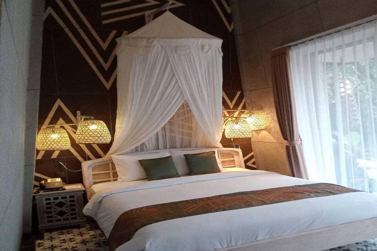 Una cama con dosel, dos lámparas de noche y una alfombra estampada.