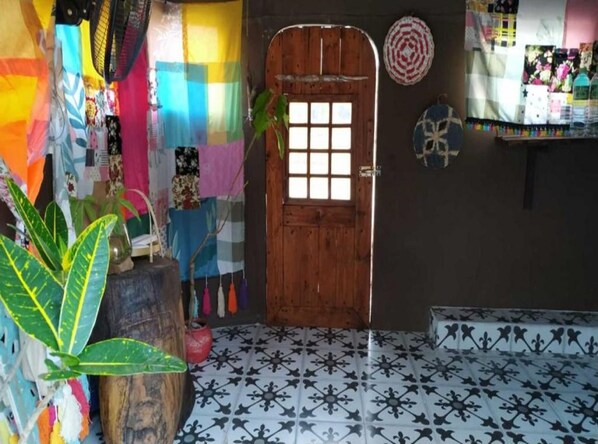 Una habitación con puerta de madera, tejidos coloridos, una planta en maceta y baldosas de suelo estampadas.