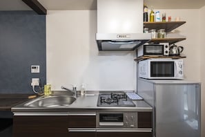 A modern kitchen with a stainless steel sink, gas stove, microwave, and built-in oven. - Shiki Homes | RURI 瑠璃 (near Umeda) (Osaka)