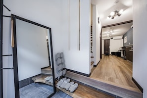 A modern hotel interior with a staircase leading to a second floor, a hallway with a mirror, and a kitchen area. - Shiki Homes | RURI 瑠璃 (near Umeda) (Osaka)