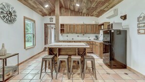 Una cocina con armarios de madera, una isla central con taburetes, un refrigerador y un reloj en la pared.