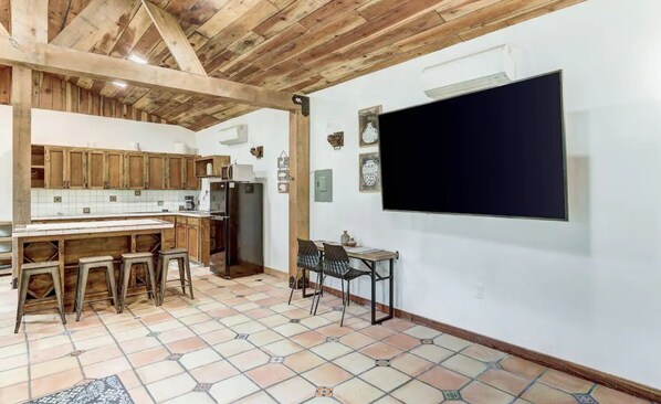 Una cocina con armarios de madera, un refrigerador, piso de baldosas y un comedor con una mesa y sillas.