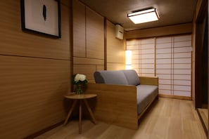 A traditional Japanese room with a low wooden bed, a small round table with a vase of flowers, and a sliding shoji screen door. - Shiki Homes | Ikkō 10  一耕の宿 10 (Kyoto)