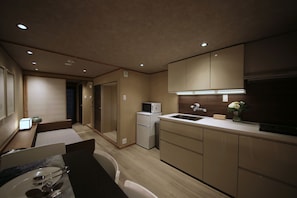 Cocina compacta con microondas, refrigerador y lavabo. Hay una zona de comedor con mesa y sillas.