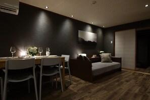 A modern dining area with a wooden table, white chairs, and a small side table with a lamp.