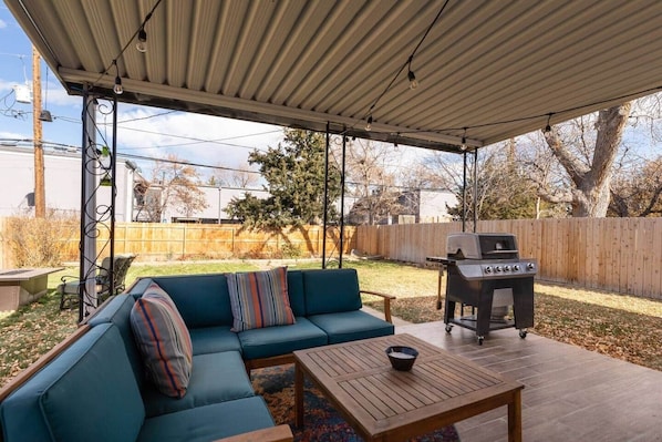 A covered patio with a sectional sofa, a grill, and a table.