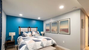 Um quarto com cama, mesas de cabeceira, um apoio para objetos e três quadros na parede.