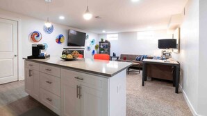 Cozinha moderna com ilha central, área de jantar com mesa e cadeiras, sofá e TV fixada na parede.