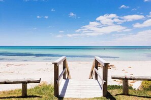A wooden boardwalk leading to a beach with clear turquoise water and a clear sky.