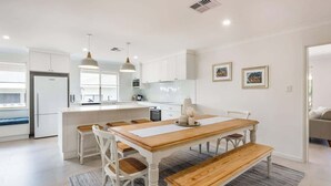Een moderne keuken met witte kastjes, een houten eettafel en hanglampen.