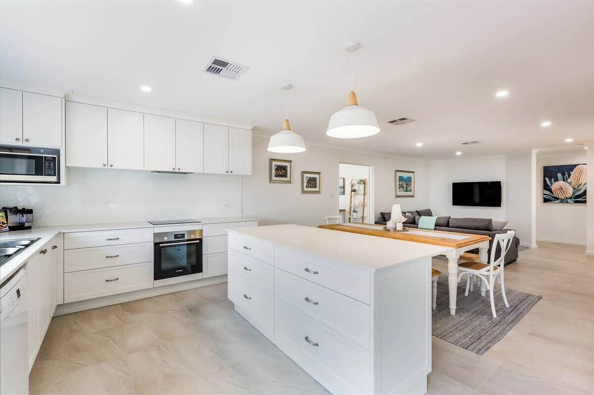 A modern kitchen with white cabinets, a central island, pendant lighting, and a dining area with a table and chairs.