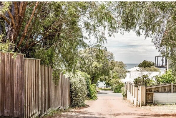 A residential street with a wooden fence, a pathway, and a view of a house with a white exterior.