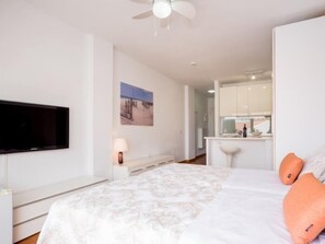 Une chambre à coucher avec un lit, un téléviseur fixé au mur, un bureau avec une lampe, et une salle de bain visible au fond.