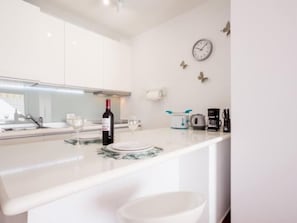 A modern kitchen with white cabinets, a marble countertop, a wine bottle, glasses, a coffee maker, and a toaster.