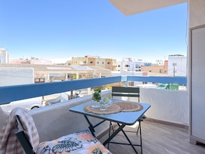 Un balcón con una mesa lista para dos personas, una silla y vistas de la ciudad.