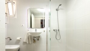 Un baño moderno con inodoro, lavabo, espejo y ducha.