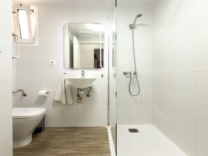 Un baño moderno con inodoro, lavabo, espejo y ducha.