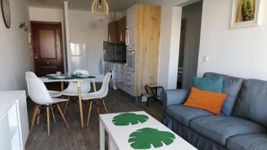 Ein modernes Wohnzimmer mit einem grauen Sofa, einem weißen Couchtisch mit grünem Blattmuster und einem Essbereich mit weißen Stühlen und einem Tisch.