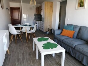 A modern living room with a grey sofa, a white coffee table with a green leaf design, and a dining area with white chairs and a table.