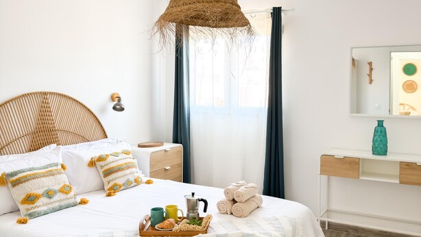 Un dormitorio ordenado con cama, mesita de noche y una lámpara colgante.