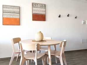 A dining area with a round wooden table, four chairs, and two wall-mounted artworks. - Elcano by Best Holidays Fuerteventura (Corralejo)