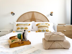 A neatly made bed with decorative pillows, a coffee maker, and a tray with a croissant and coffee cup.