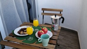 Ein Frühstück auf einem Holztisch mit grüner Tischdecke, bestehend aus Gebäck, zwei Gläsern Orangensaft, einer Schale mit Äpfeln und einer Kaffeekanne.