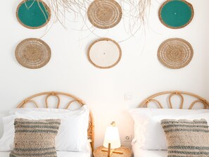 Una habitación con dos camas, una lámpara de noche y adornos tejidos en la pared.