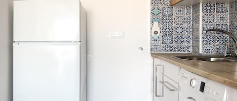 A compact kitchen with a white refrigerator, a washing machine, and a sink with a patterned backsplash.