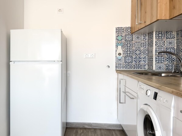 Cocina compacta con refrigerador blanco, lavadora y pileta con salpicadero estampado.
