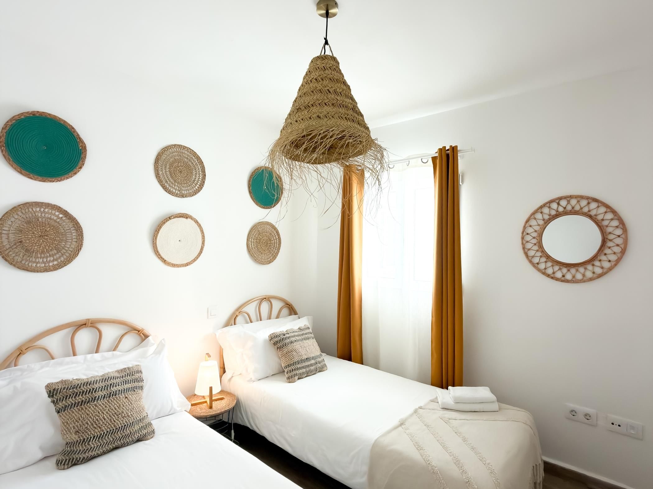Un dormitorio con dos camas, una lámpara colgante tejida y adornos textiles en la pared.