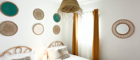 Un dormitorio con dos camas, una lámpara colgante tejida y adornos textiles en la pared.