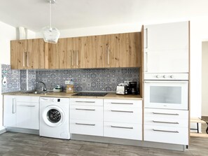 Eine moderne Küche mit Holzschränken, einer Waschmaschine, einer Kaffeemaschine und einem Einbauofen.