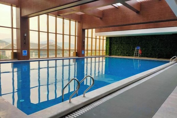 Una piscina interior con paredes de vidrio transparente, una escalera y vistas al exterior.