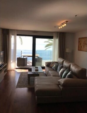 Relax in this stylish living room with a comfortable sofa, flat-screen TV, and sliding glass door leading to a balcony with ocean views.