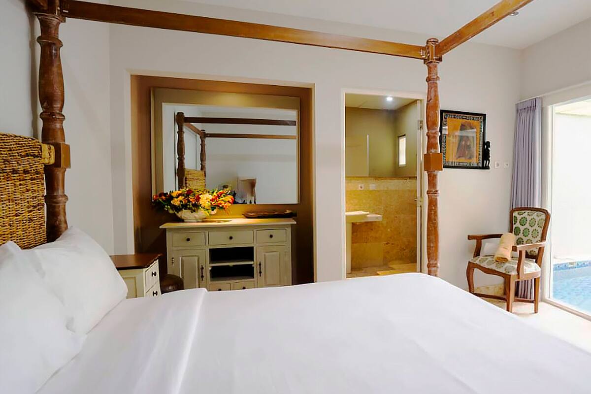 Quarto com cama de dossel, penteadeira com espelho, uma cadeira e vista para o exterior.