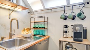 A modern kitchen with a stainless steel sink, a bowl of fruit, a coffee machine, and a rack with mugs and glasses. - 2 Mi to Dtwn: Boston Apartment Near Beaches! (Boston)