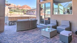 A covered patio with wicker furniture, a glass coffee table, and a view of red rock formations. - Sedona Sanctuary w/ Hot Tub, Fire Pit & Grill (Sedona)